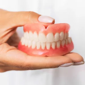 Dentures in Stuart — hand holding a full set of dentures with pink gums and white teeth